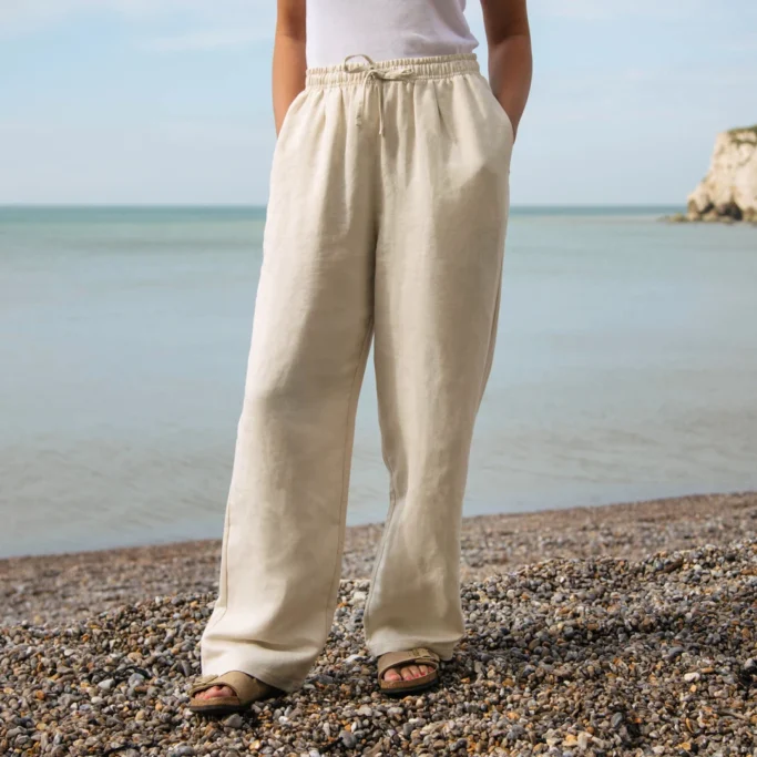 Traveller wearing loose cream linen trousers and sandals beside the sea