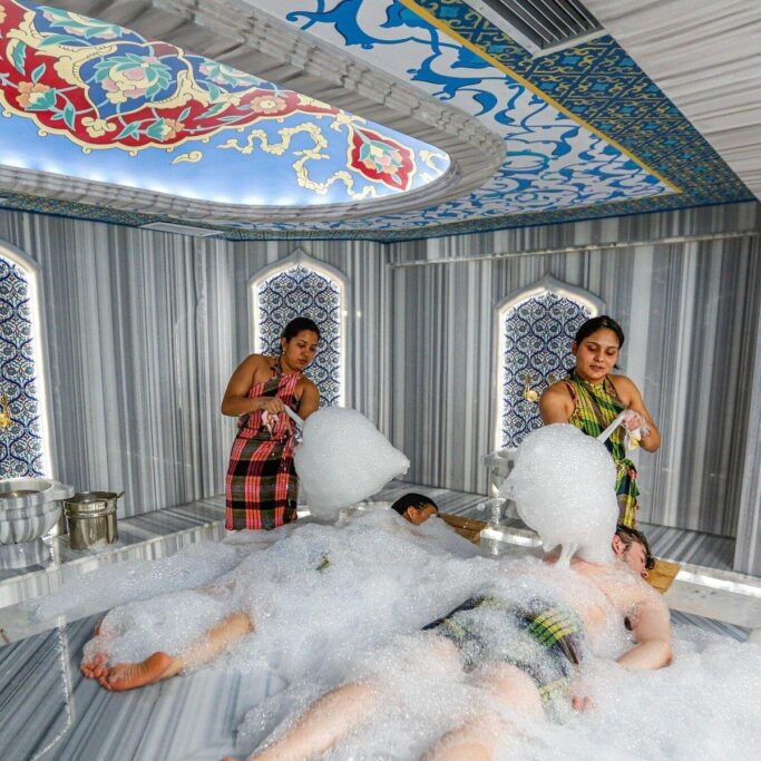 Foam massage in an Istanbul Turkish hammam with guests lying on warm marble